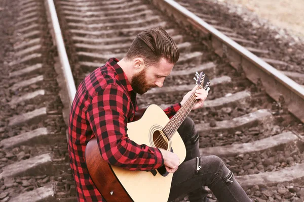 Hombre guapo tocando la guitarra en el ferrocarril — Foto de Stock