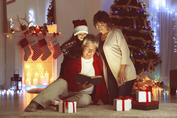 小さな女の子と彼女の祖父母を読んでクリスマスに装飾されたリビング ルームの予約します。 — ストック写真