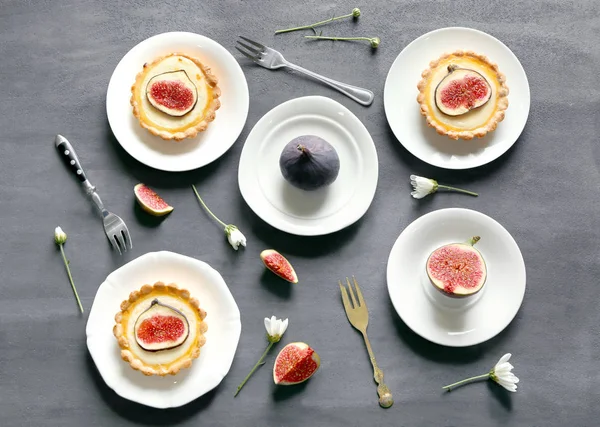Тарелки с вкусными инжирными тортами и свежими фруктами на сером фоне, вид сверху — стоковое фото
