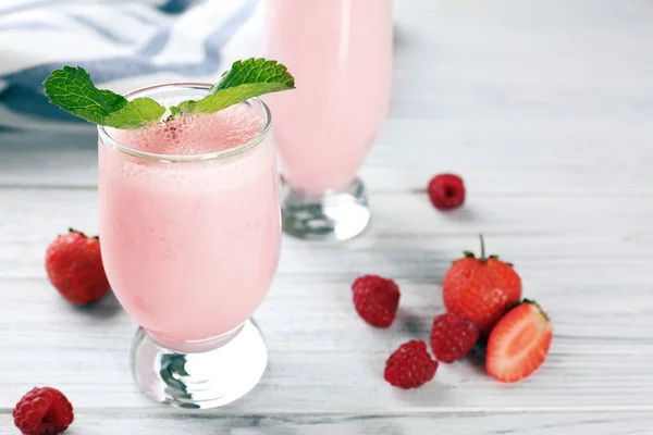 Стакан вкусного молочного коктейля и свежих ягод на белом деревянном фоне — стоковое фото