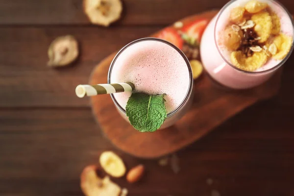 Glasses of delicious milkshake with berries and flakes on wooden board, closeup — Stock Photo, Image