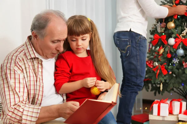 Homem idoso lendo livro com sua neta na sala de estar decorada para o Natal — Fotografia de Stock