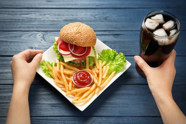 Woman with burger, french fries and cola on wooden background — Stock Photo, Image