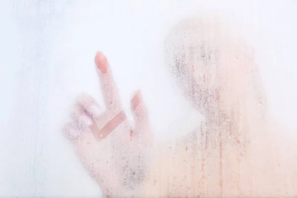 Beautiful young woman drawing on weeping glass of  shower door — Stock Photo, Image