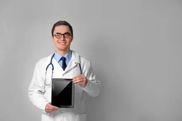 Junger Arzt mit Tablette auf grauem Wandhintergrund — Stockfoto