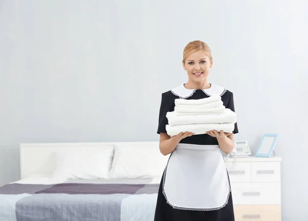 Camareira segurando pilha de toalhas limpas no quarto — Fotografia de Stock