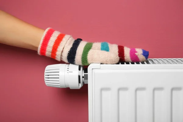 Mão feminina em mitene quente na bateria de aquecimento no fundo rosa — Fotografia de Stock