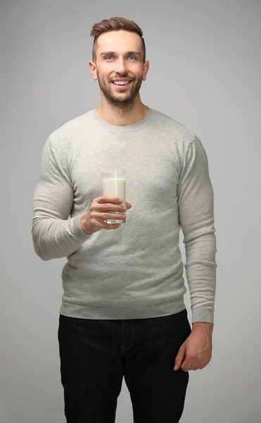 Молодой человек со стаканом свежего молока на сером фоне — стоковое фото