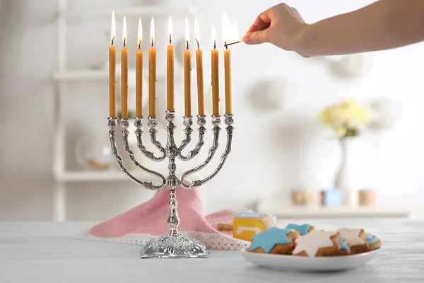 Female hand applying match to candles in menorah on wooden table. Hanukkah concept — Stock Photo, Image