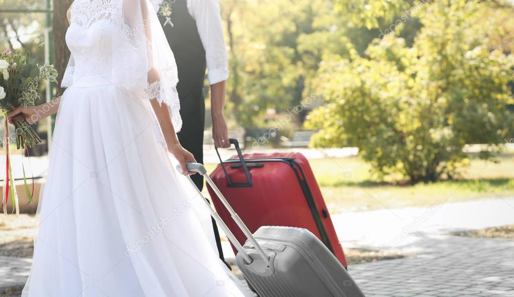 Bride and groom with big suitcases walking outdoors