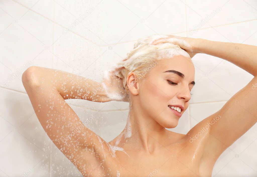 Beautiful young woman washing head in shower