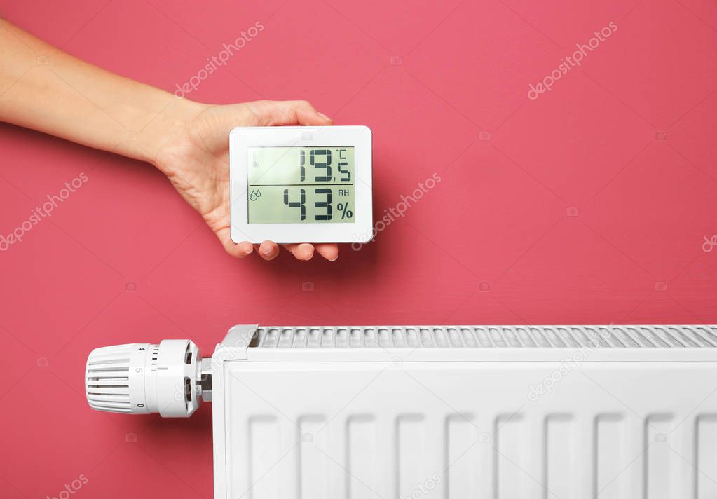 Female hand holding electronic thermometer near heating battery