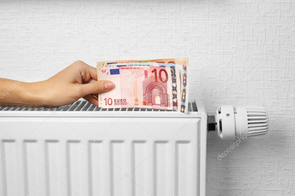 Woman holding money on heating battery