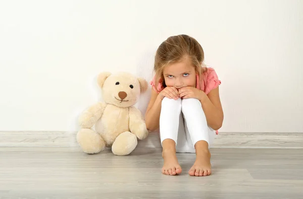 Сумна дівчинка з плюшевим ведмедем сидить на підлозі — стокове фото