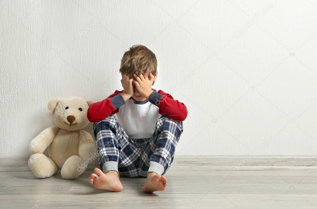 Crying little boy with teddy bear on floor in empty room
