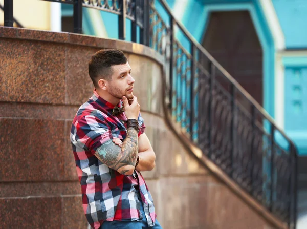 Jovem tatuado homem posando no embaçado edifício fundo — Fotografia de Stock