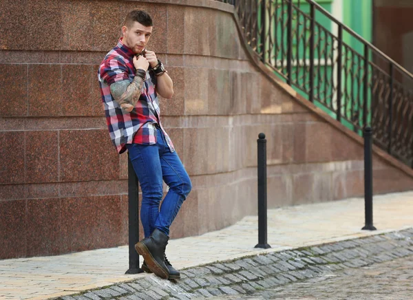 Jovem tatuado homem posando no embaçado edifício fundo — Fotografia de Stock