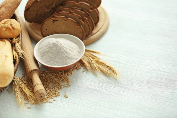 De sneetjes brood met tarwemeel, spikes en korrels op witte tafel — Stockfoto