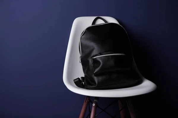 Черный кожаный рюкзак на белом стуле и темном фоне — стоковое фото