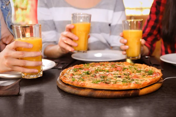 Amigos sentados a la mesa con jugo de naranja y sabrosa pizza, vista de cerca — Foto de Stock