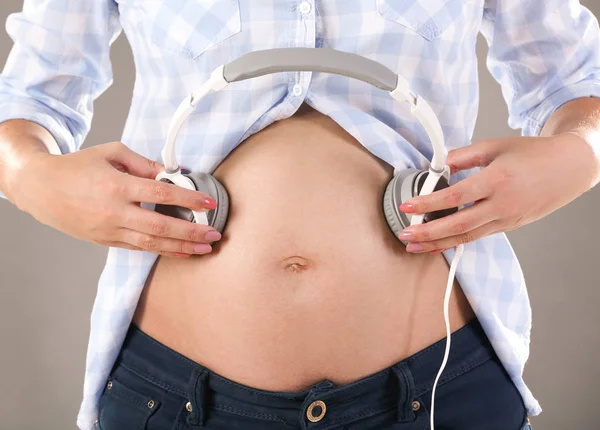 Gravid kvinna med hörlurar på magen — Stockfoto