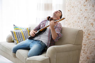 Genç adam heyecanla hafif bir odada elektro gitar çalmak kulaklık