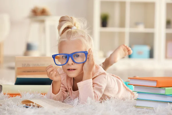 Küçük kız gözlük ile halı üzerinde pek çok kitap — Stok fotoğraf