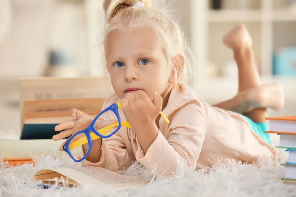 Menina pequena com óculos com muitos livros no tapete — Fotografia de Stock