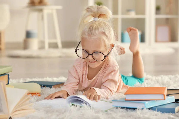 Liten flicka i glasögon med många böcker på mattan — Stockfoto