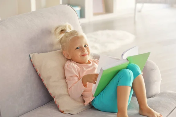 Маленька дівчинка читає книгу на дивані — стокове фото
