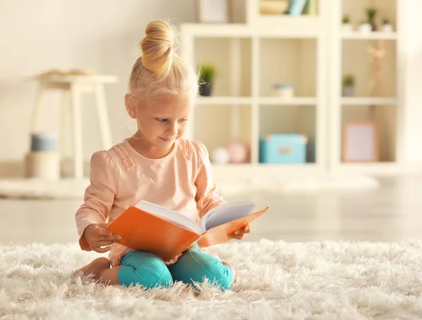 Niña leyendo libro sobre alfombra — Foto de Stock