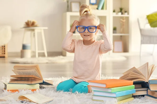 Menina pequena em óculos com muitos livros no tapete — Fotografia de Stock