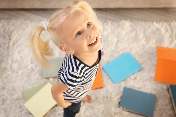 Piccola ragazza con mucchio di libri su tappeto a casa — Foto Stock