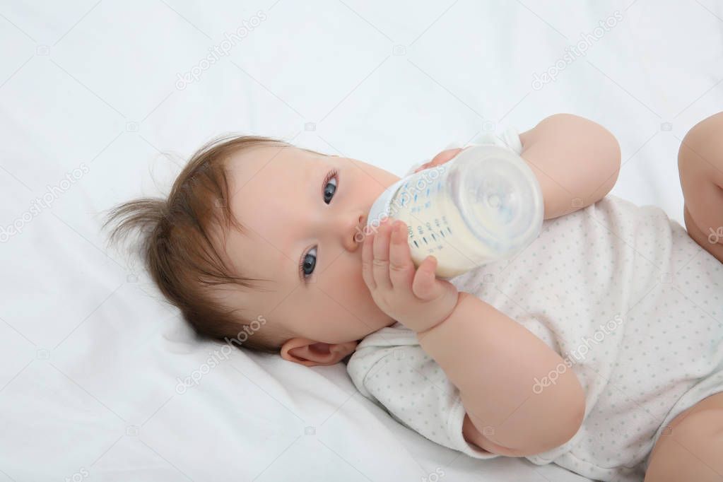 Cute baby with bottle on bed