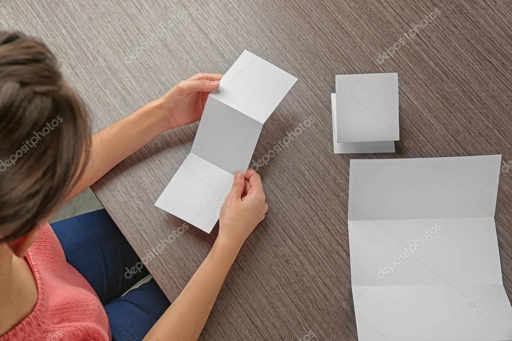 Woman sitting at wooden table with blank booklets