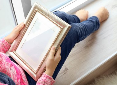 Fotoğraf çerçevesi tutarak ve pencere oturan genç kız