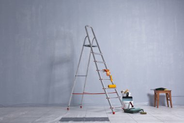 Boş odada tamirat yapmak için merdiven, boya ve aletler