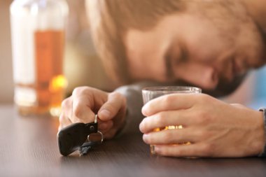 Barda oturan adam arabanın anahtarı ve bir bardak alkollü içecekle, yakın plan. İçkili araba kullanma.