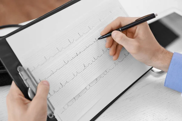 Manliga läkare att göra anteckningar på kardiogram Stockbild
