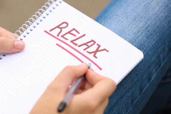 Giovane donna che scrive parola "rilassarsi" nel quaderno — Foto Stock