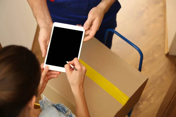 Young woman appending signature after receiving parcel from courier at home, closeup