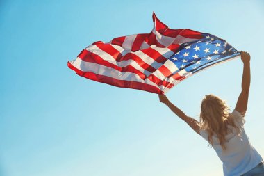 Amerikan bayrağı mavi gökyüzü arka plan üzerinde tutan genç kadın