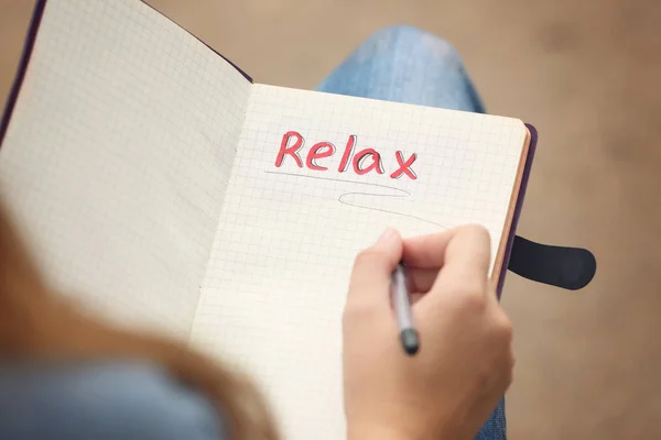 Mujer joven escribiendo palabra "relajarse" en el cuaderno —  Fotos de Stock