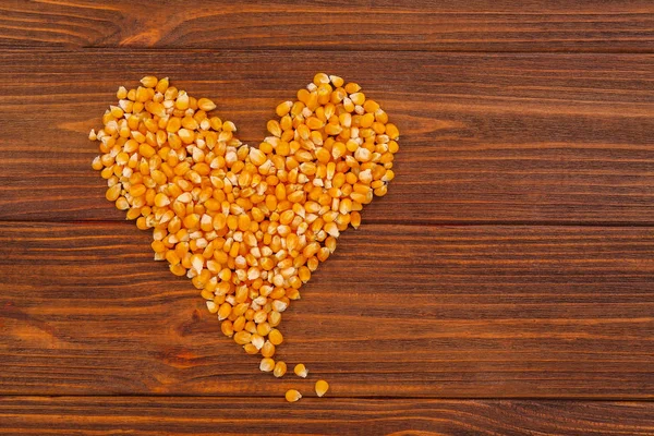 Heart made of maize grains on wooden background, top view