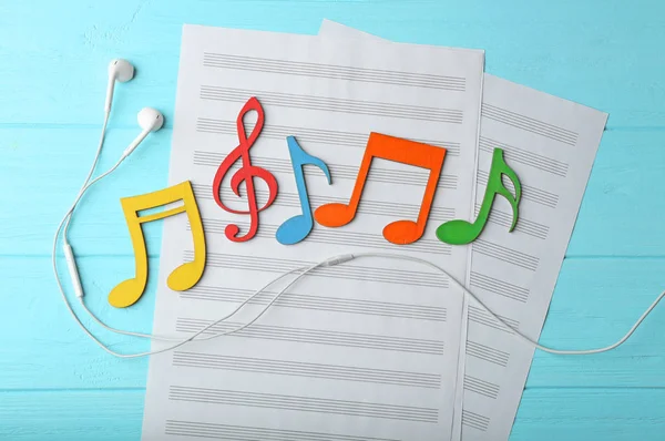 Earphones, music notes and sheets of paper on color wooden background