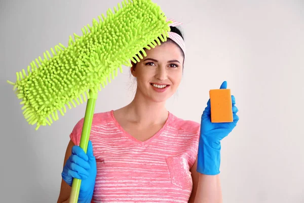 Happy young cleaner with dust mop and sponge on light background — Stock Photo, Image