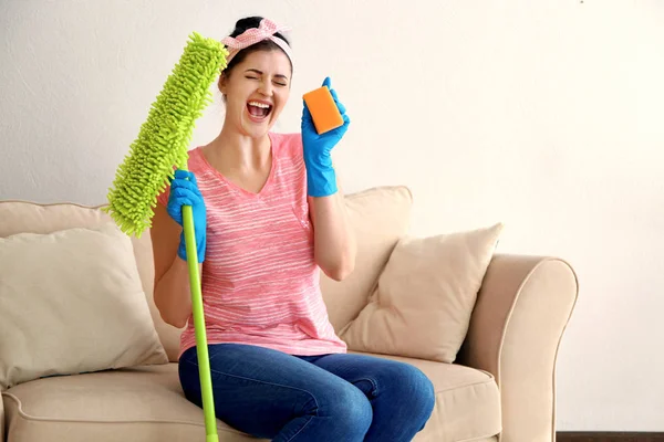 Szczęśliwy młody cleaner z mopa i gąbki, siedząc na kanapie — Zdjęcie stockowe