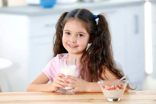 Menina bonito com leite e pequeno-almoço saudável à mesa na cozinha — Fotografia de Stock