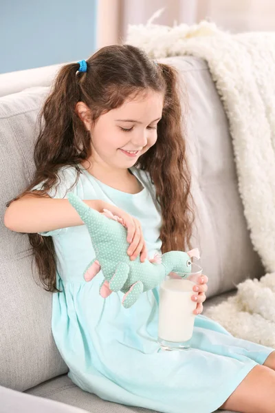 Menina bonito alimentando dinossauro brinquedo com leite — Fotografia de Stock