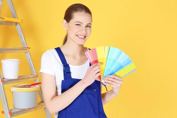 Beautiful young decorator with color samples on yellow background — Stock Photo, Image